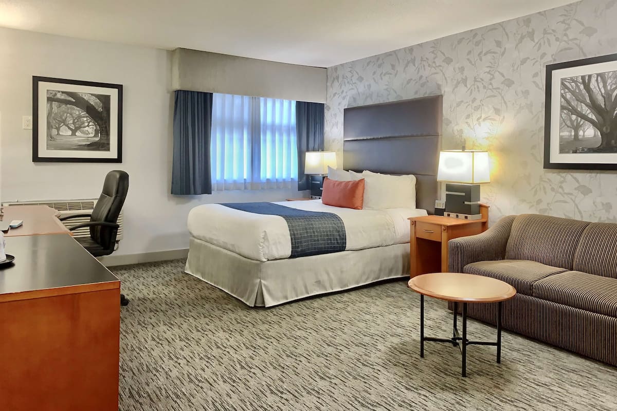 A hotel room with a bed, desk, chair, and a small table.