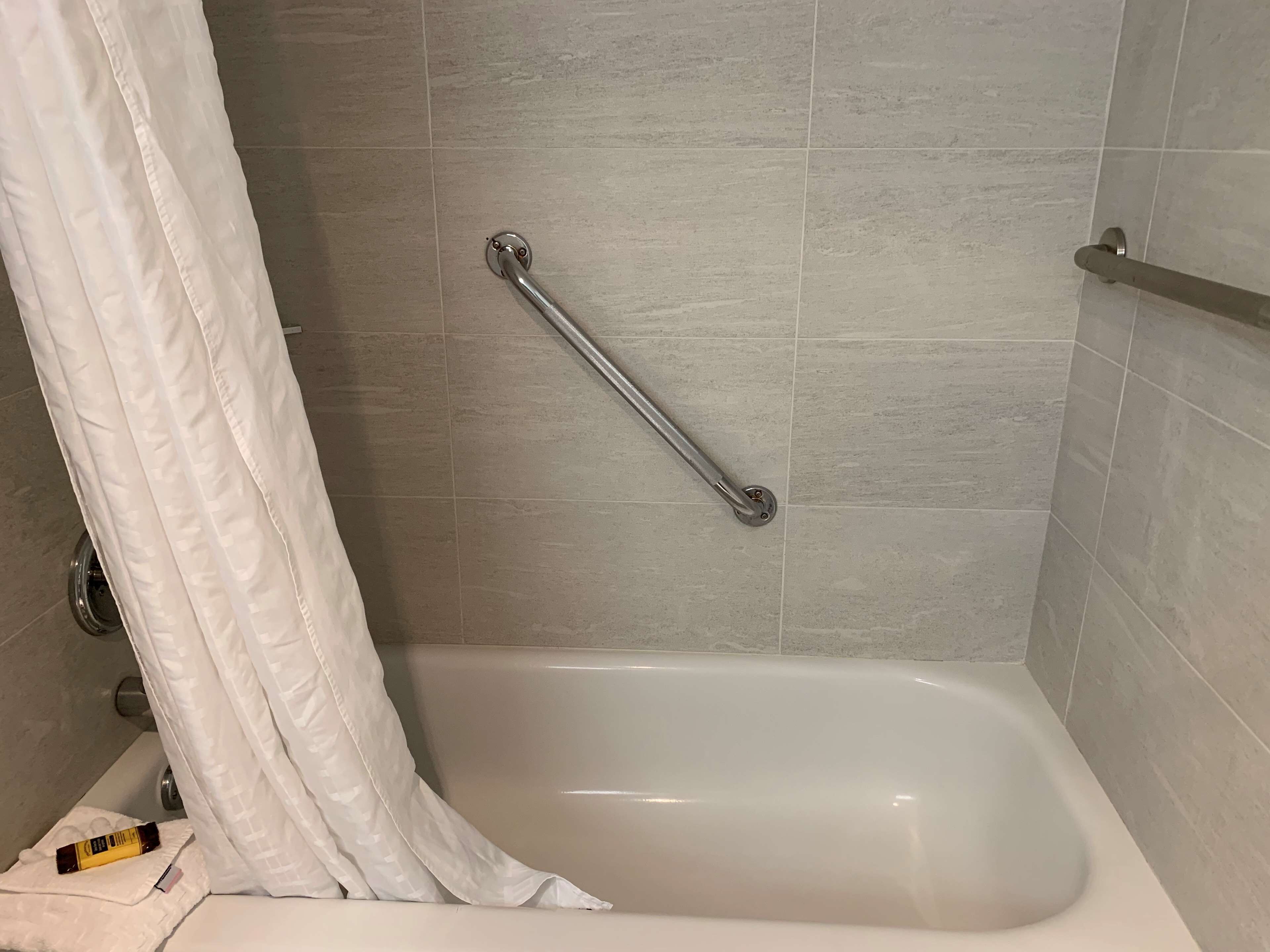 Une salle de bain avec une baignoire, une barre d’appui et un rideau de douche blanc.