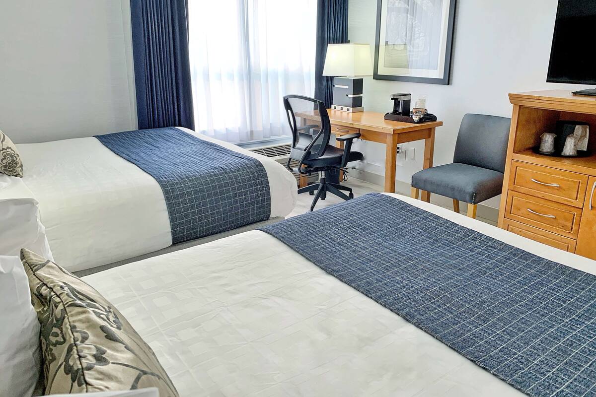 A hotel room with two beds, a desk, a chair, a television, and a cabinet.