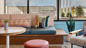 A modern living room with a colorful ceiling, a large window with a view of the outdoors, a sofa with patterned cushions, a round wooden table, and a red ottoman. - The Wayback, Pigeon Forge, A Tribute Portfolio Hotel (Pigeon Forge)