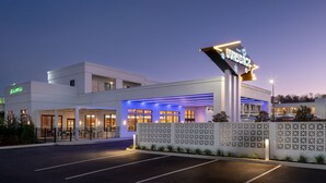 Ein modernes Hotel mit einer auffälligen Beschilderung mit dem Aufschrift "The Playback". Es verfügt über einen großzügigen Außenbereich mit überdachter Sitzgelegenheit und einem gut beleuchteten Eingang.