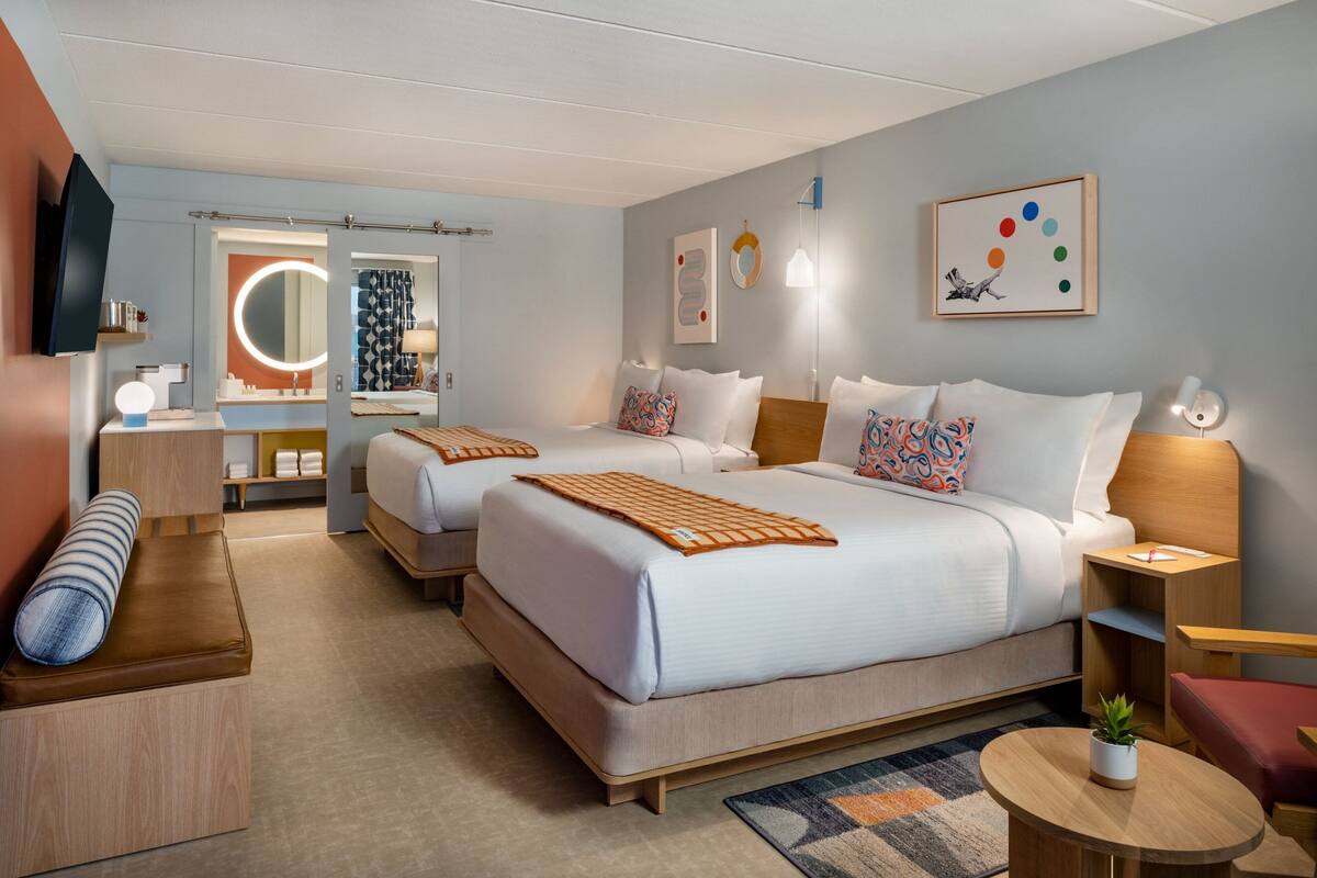 A hotel room with two beds, a TV, a bathroom, and a small seating area.