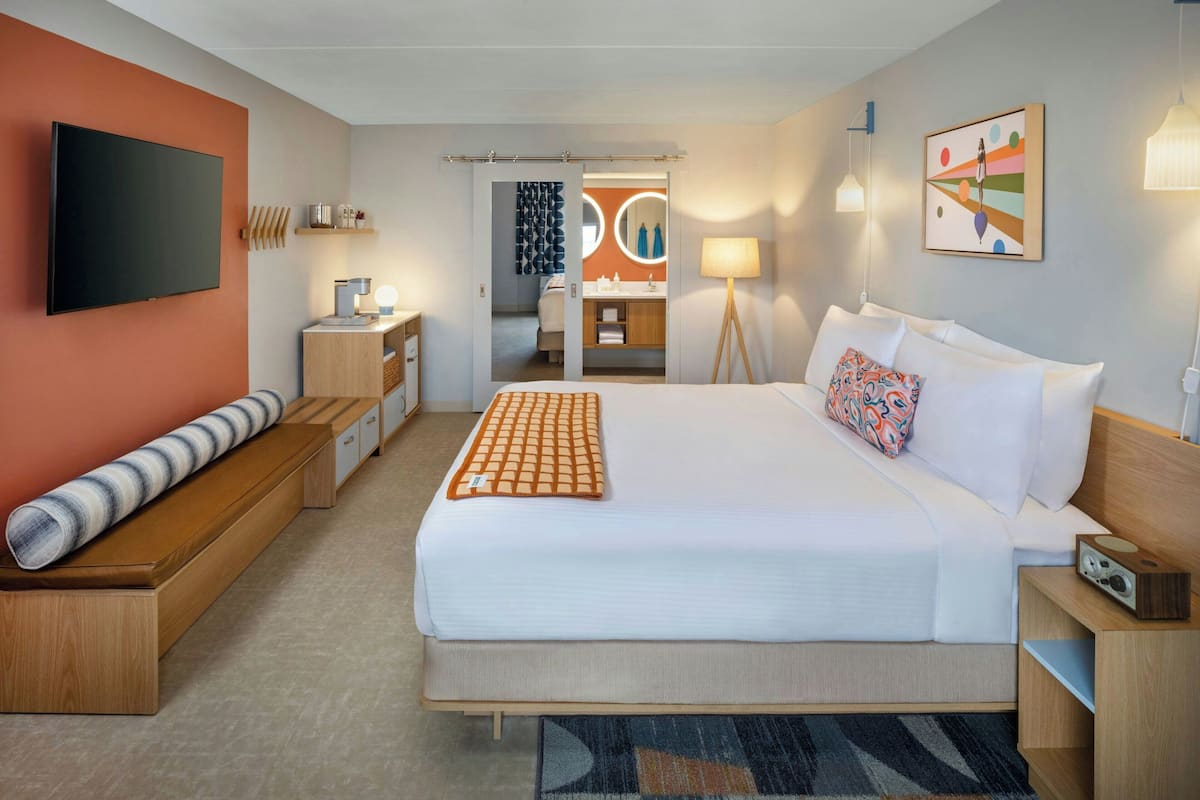 A hotel room with a large bed, a TV, a desk, and a bathroom visible through an open door.