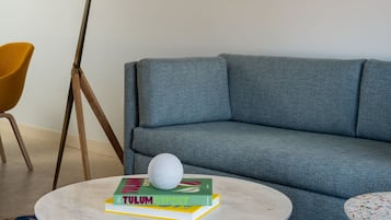 A modern living room with a grey sofa, a round wooden coffee table with books and a white spherical object, a floor lamp, and a patterned rug.