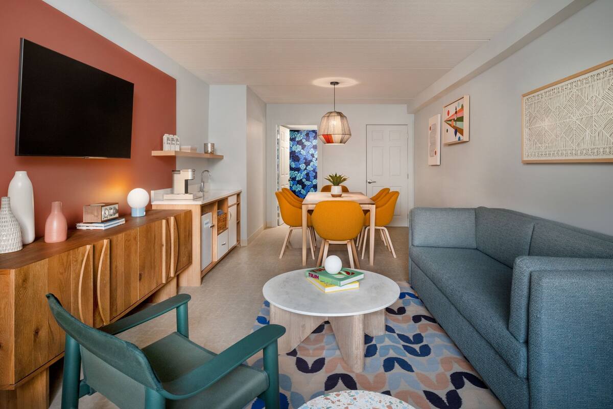 A modern living room with a sofa, a coffee table, and a TV. There is a dining area with a table and chairs.