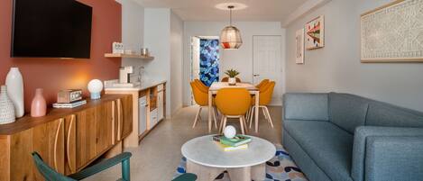 A modern living room with a sofa, a coffee table, and a TV. There is a dining area with a table and chairs.