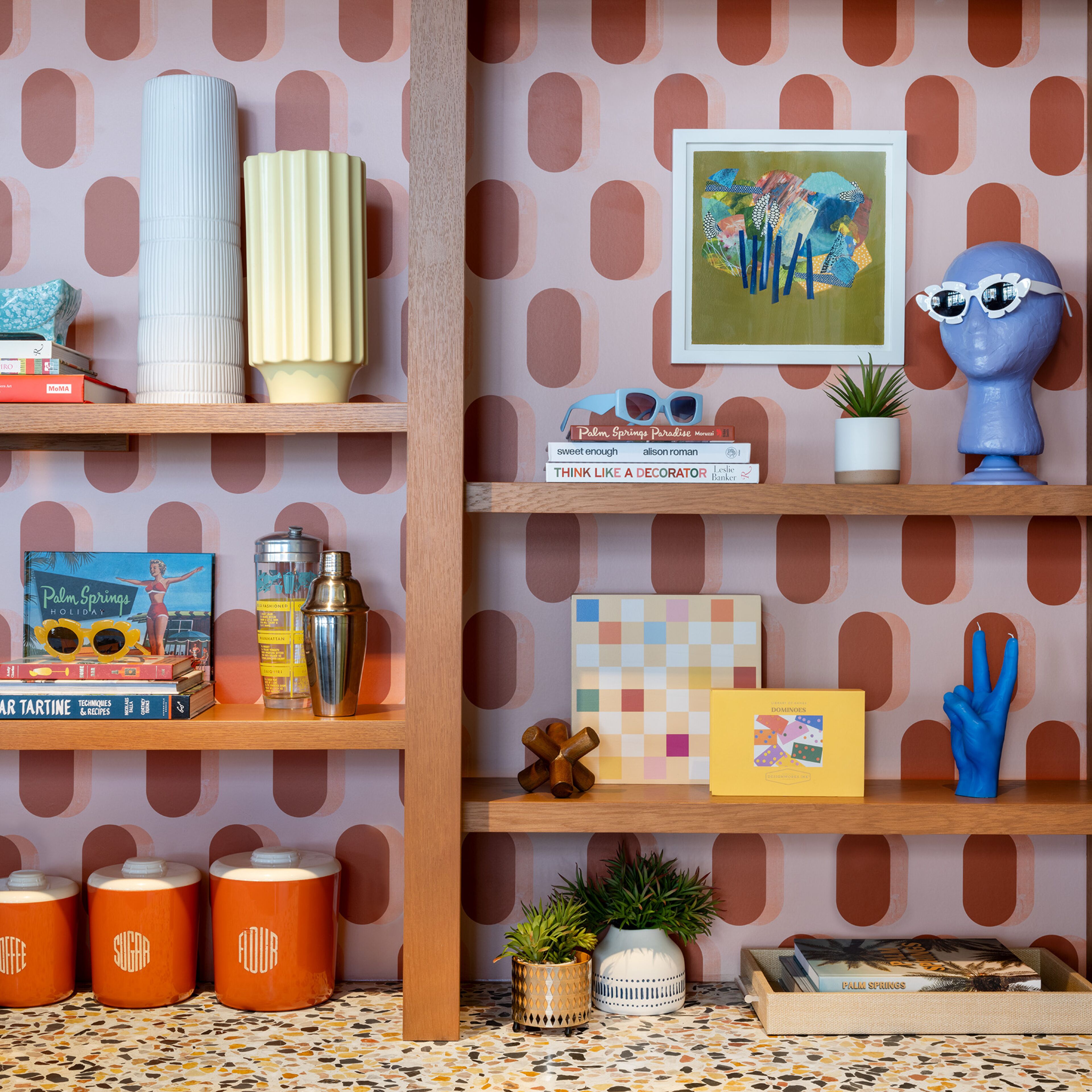 A room with a patterned wallpaper, wooden shelves, and various decorative items including books, a cocktail shaker, and a blue sculpture.