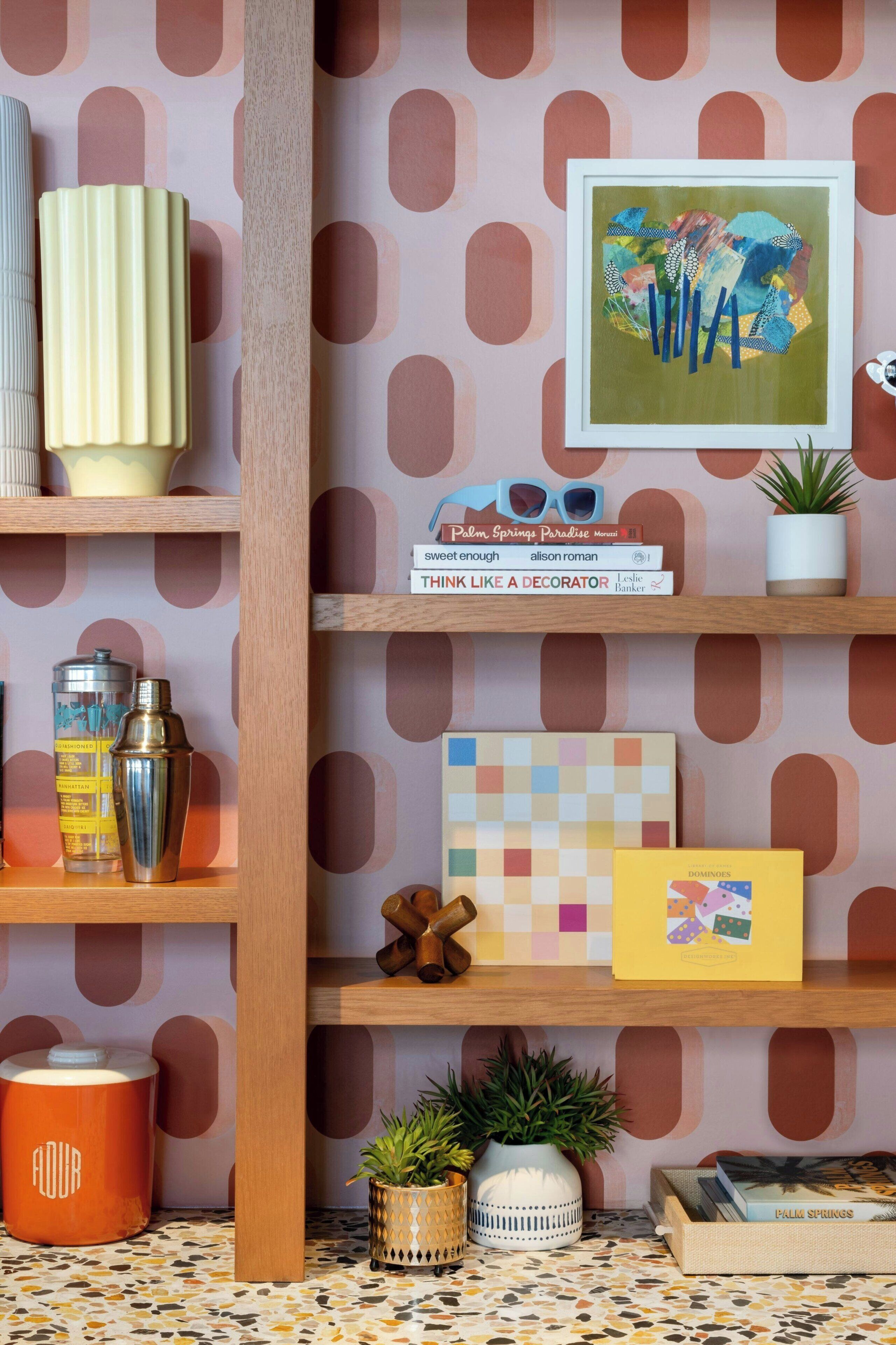 A room with a patterned wallpaper, a bookshelf with various items, a framed artwork, and a tiled floor.