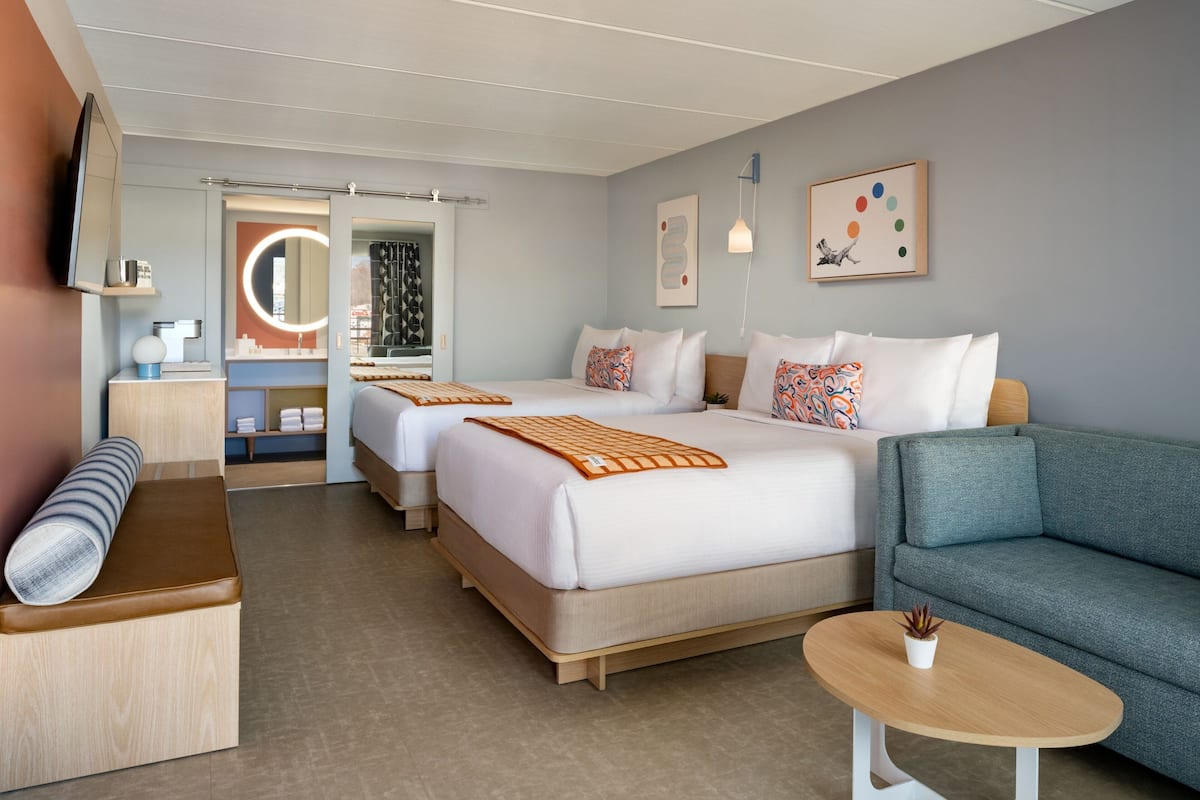 A hotel room with two beds, a sofa, a small table, a bench, and a TV.