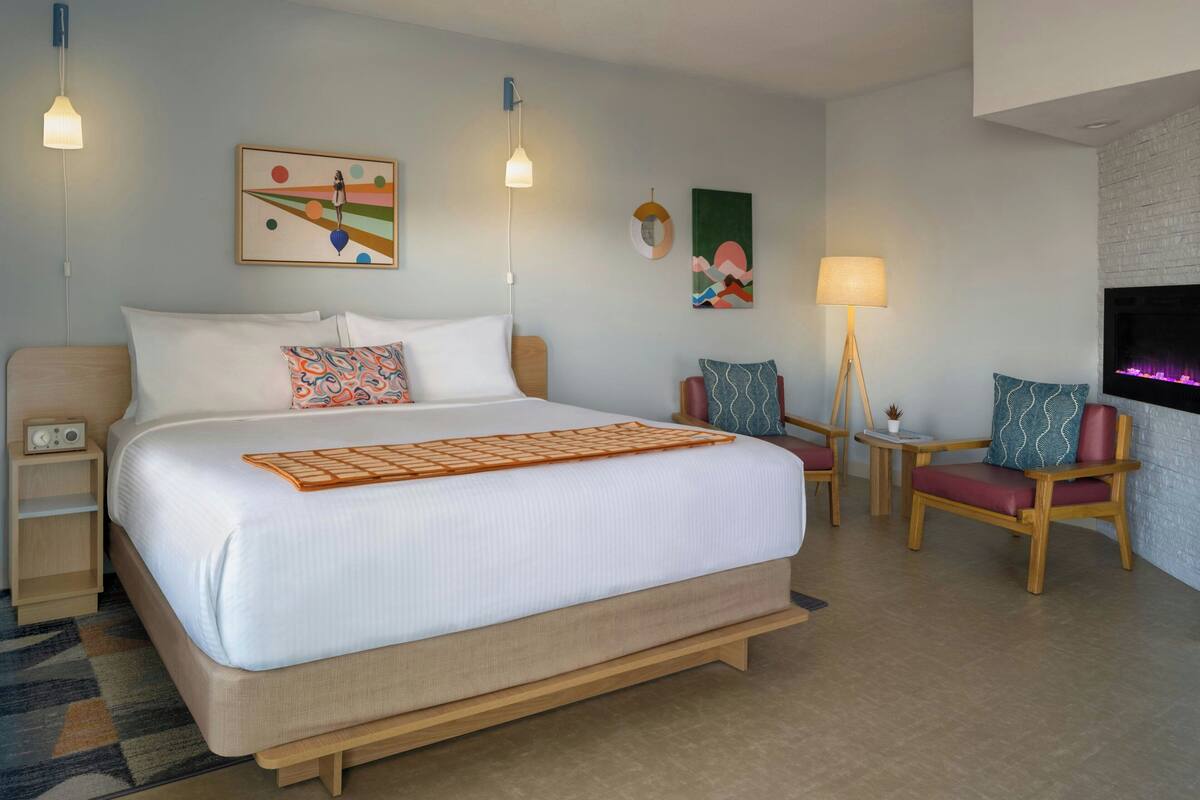A hotel room with a large bed, bedside tables, a TV, and a seating area with chairs and a small table.