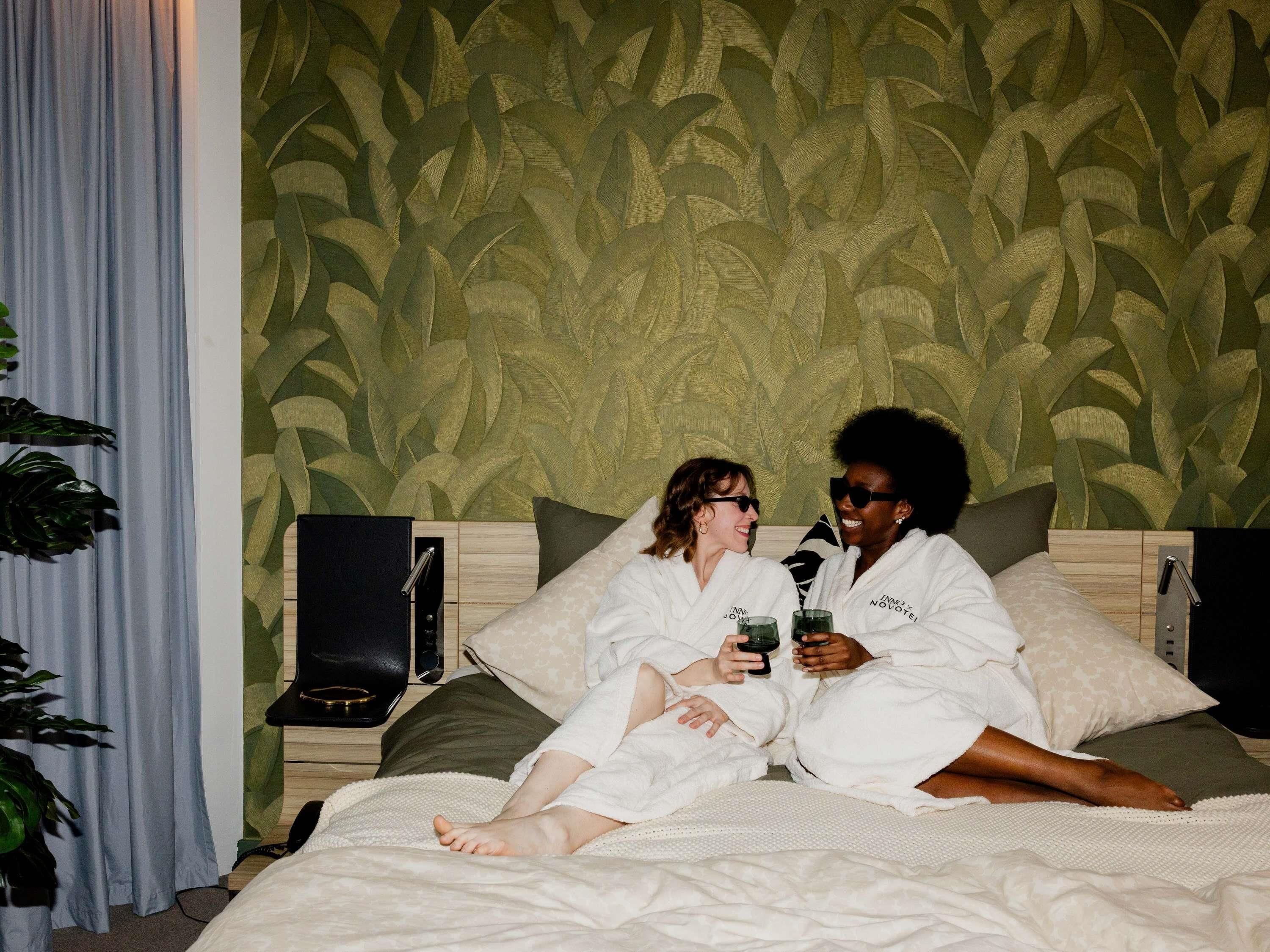 Un dormitorio con papel tapiz estampado, una cama con almohadas y una mesita de noche con un altavoz.