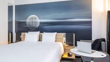 Habitación de hotel con una cama, un escritorio con una computadora portátil, un teléfono y un cuadro de un paisaje.