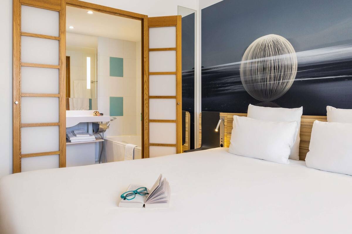 Une chambre d’hôtel avec un lit, un bureau et une salle de bain, visibles à travers une porte ouverte.