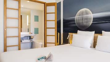 Una habitación de hotel con cama, escritorio y baño visible a través de una puerta abierta.