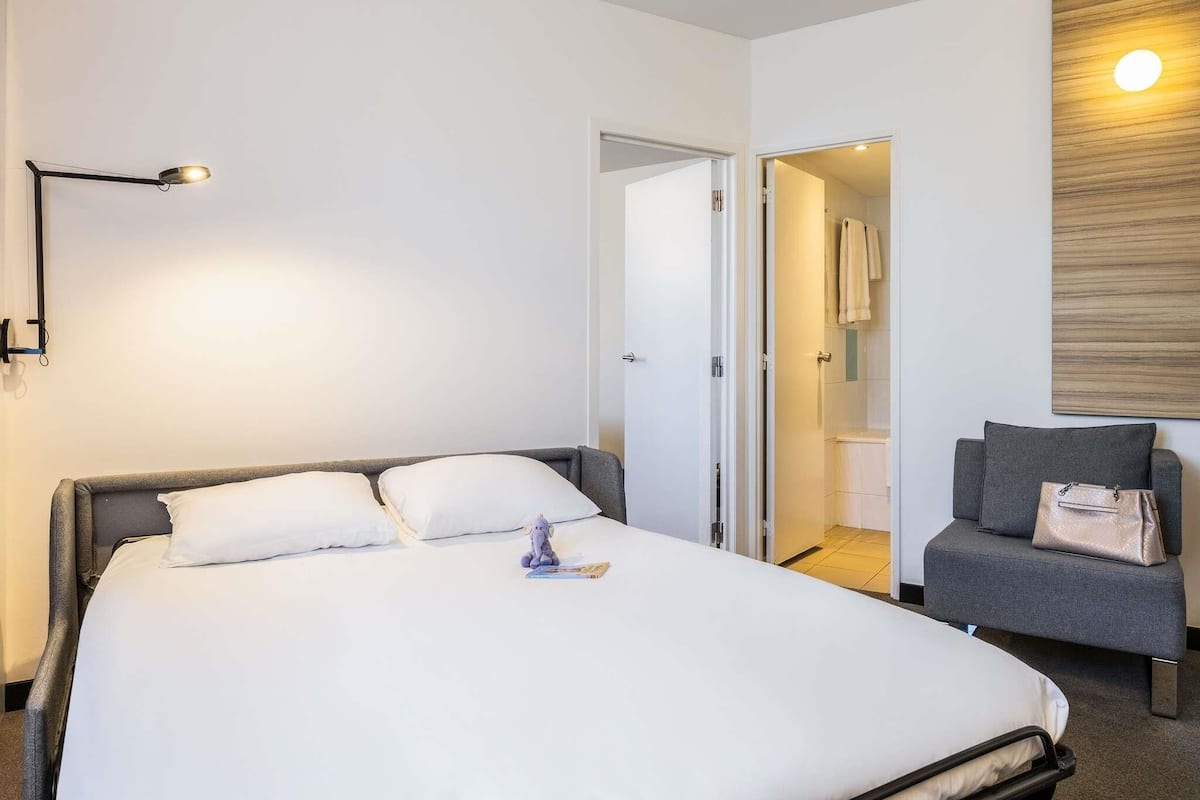 A hotel room with a large bed, a bedside table, a chair, and a wooden accent wall.