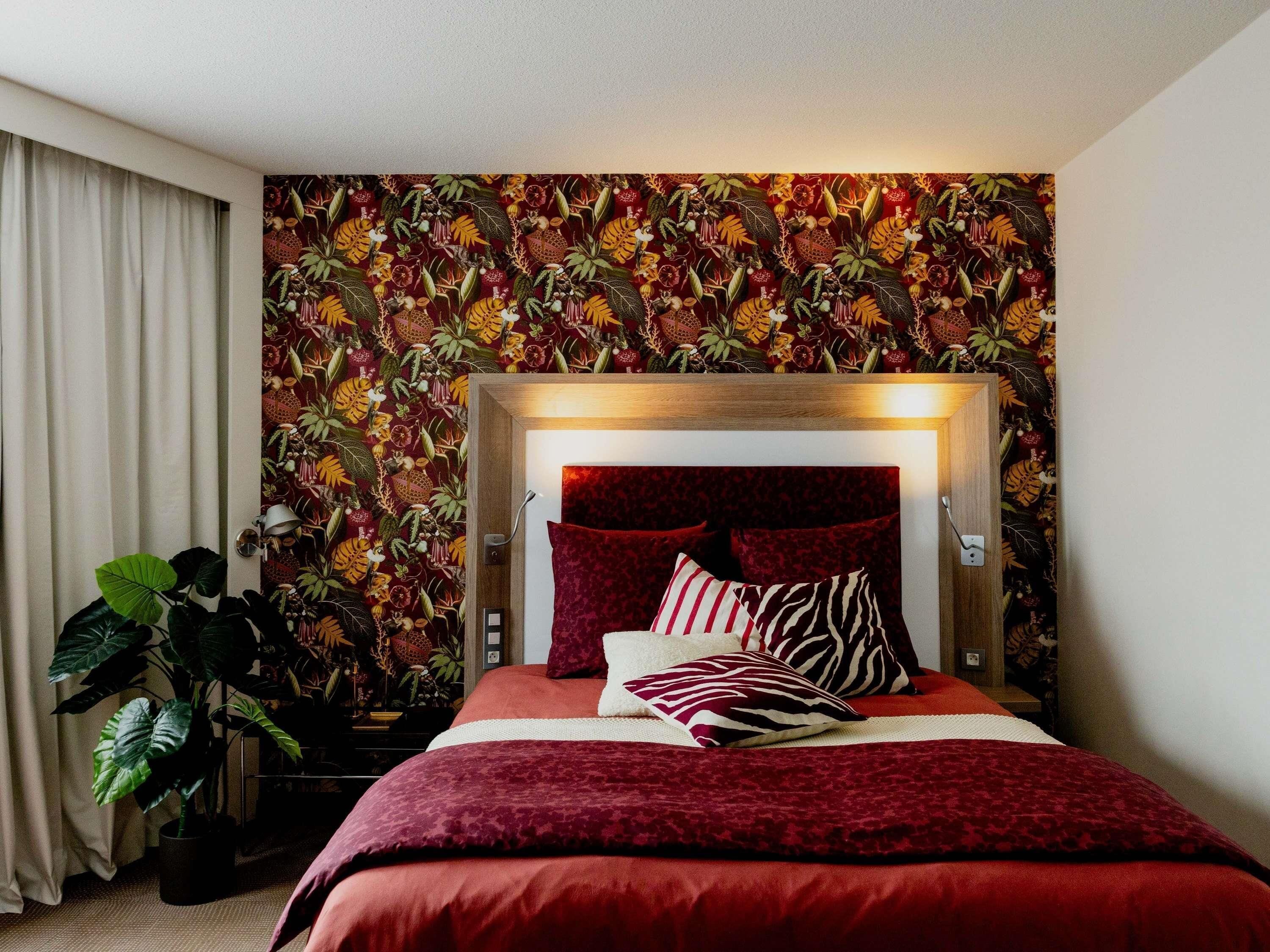 A bedroom with a bed, a headboard, and a wall with a tropical plant pattern.