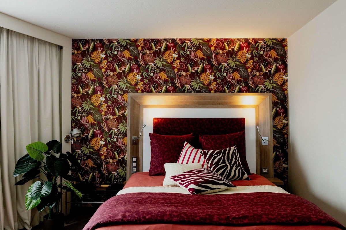 Une chambre à coucher avec un lit, une tête de lit et un mur orné d’un motif de plantes tropicales.