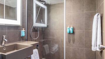 A modern bathroom with a glass-enclosed shower, a sink with a towel, and toiletries on the wall.