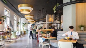 A modern restaurant with high ceilings, pendant lighting, and a mix of seating options including tables and couches. - Novotel Brussels off Grand'Place (Brussels)