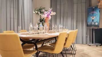 Un salón de conferencias con una mesa redonda, sillas amarillas, un centro de mesa floral, botellas de agua y un cartel en la pared.
