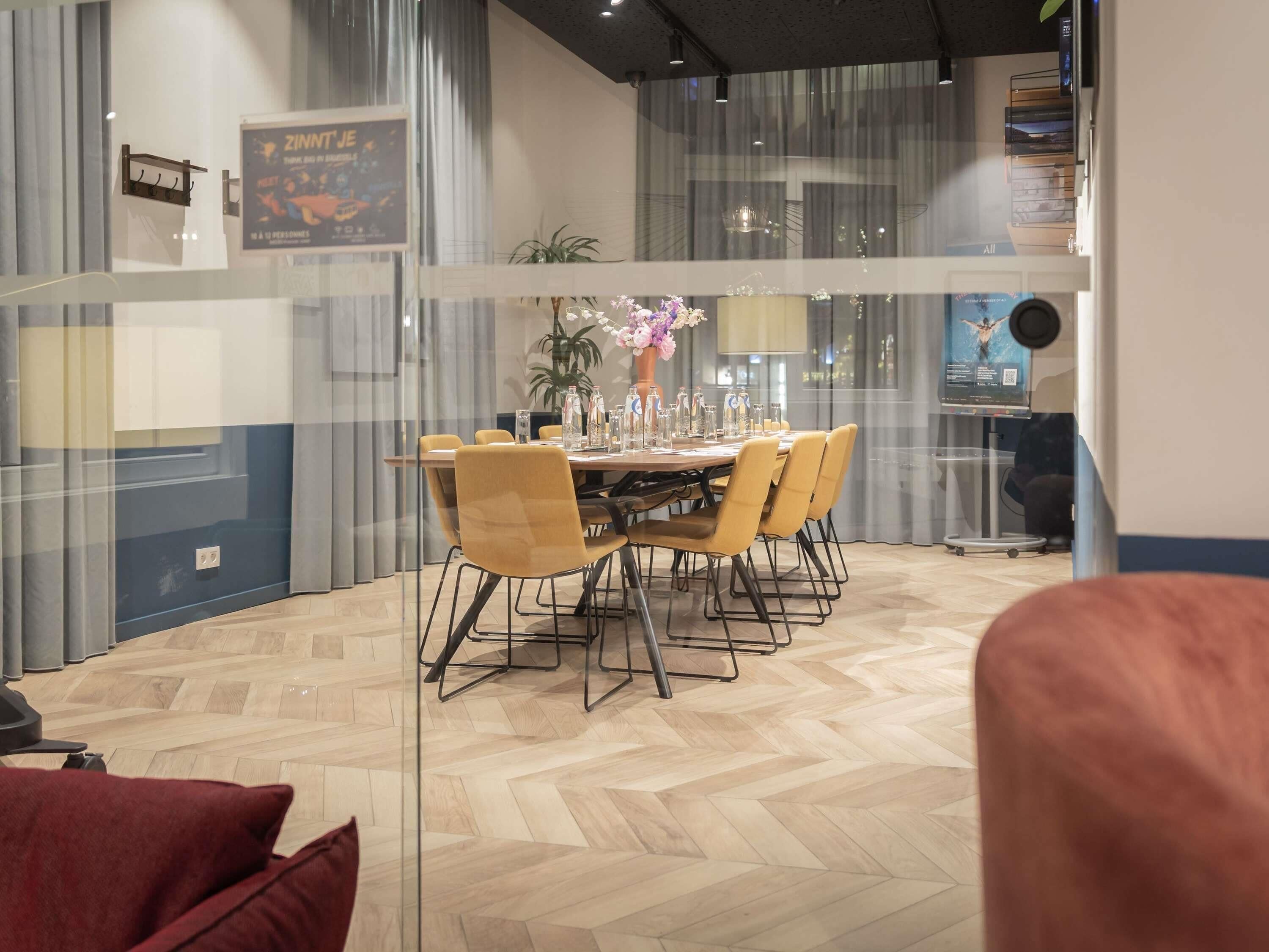 A modern dining area with a glass partition, a wooden table, and yellow chairs.