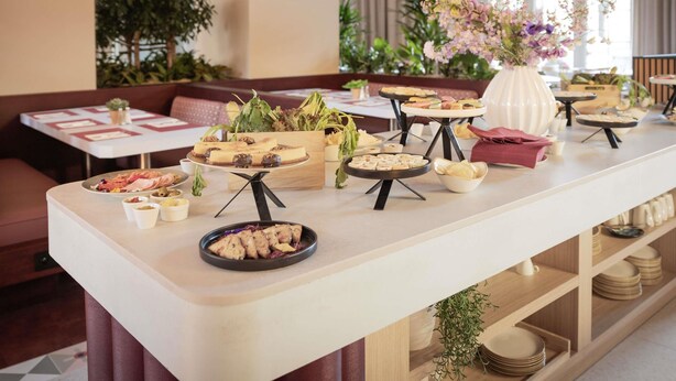 A buffet setup with various food items and a floral centerpiece in a well-lit dining area with seating and natural light. - Novotel Brussels off Grand'Place (Brussels)