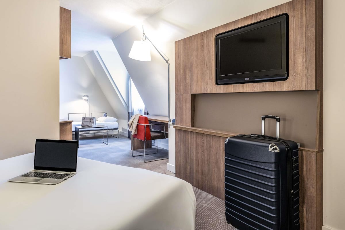 Une chambre d’hôtel avec un lit, un bureau, un ordinateur portable, une télévision et une valise.