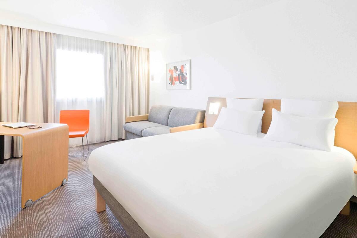 A hotel room with a large bed, a desk, a chair, and a sofa.