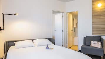 A hotel room with a large bed, a bedside lamp, a chair with a handbag, and a wooden wall panel.