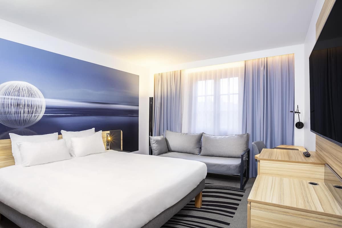 Une chambre d’hôtel moderne avec un grand lit, un canapé, un bureau et une fresque murale.