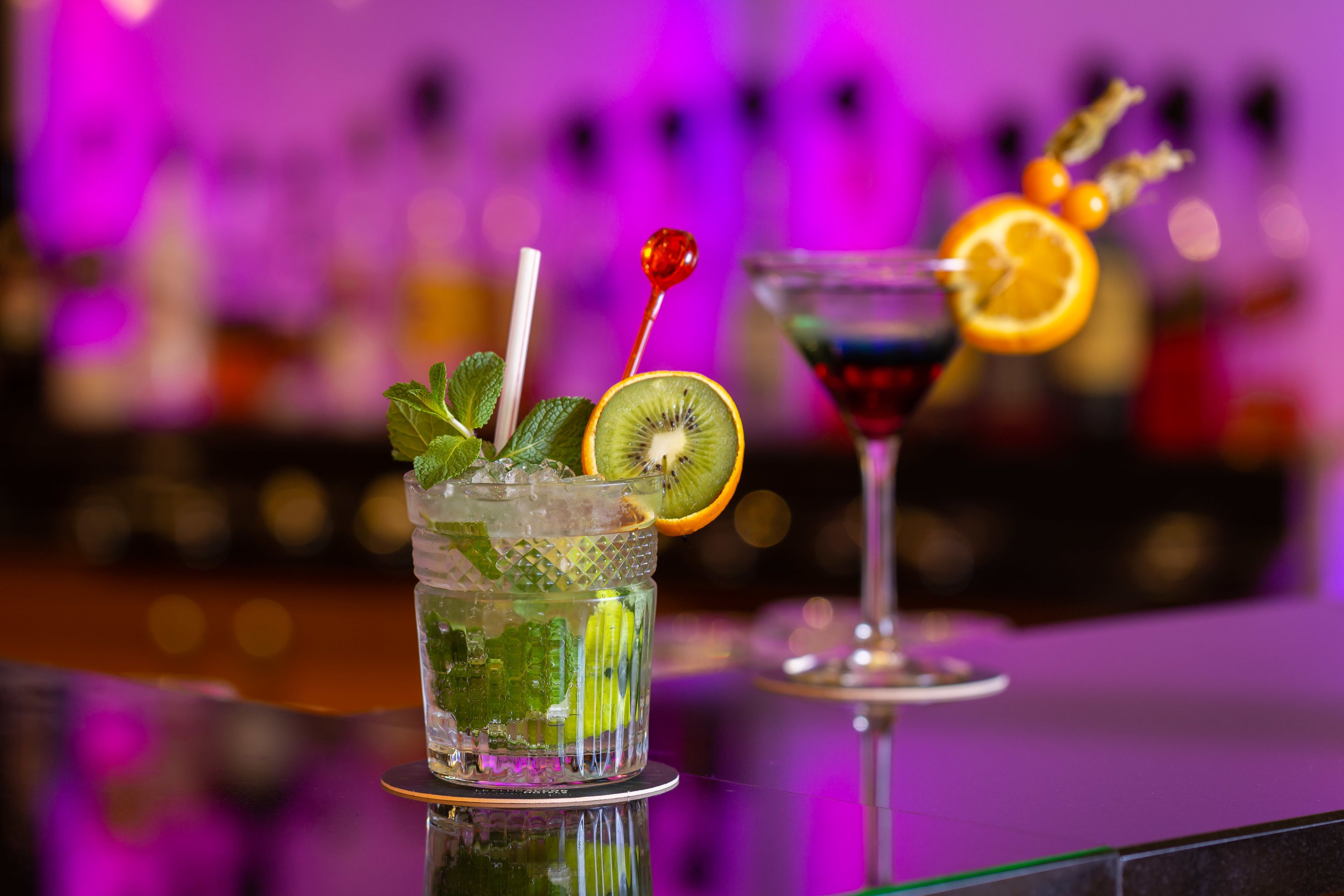 Two cocktails with garnishes on a bar counter.