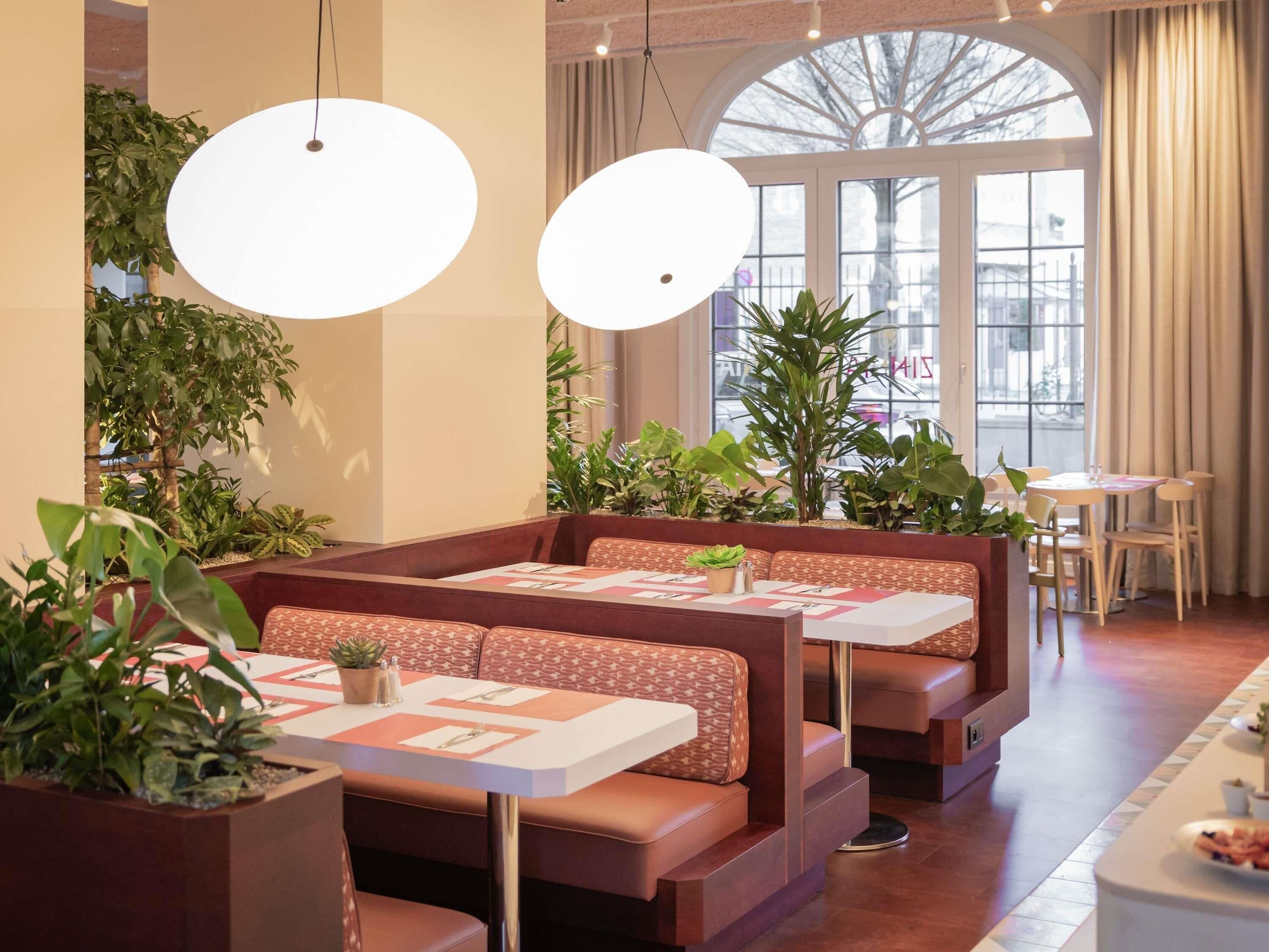 Een restaurant met zitbanken, tafels met menukaarten, potplanten en grote ramen.