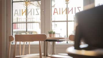 A café interior with wooden chairs and tables, large windows with a view of the street, and a sign with the word "SINS" partially visible.