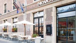 A brick building with 'NOVOTEL' signage, outdoor seating with umbrellas, and a storefront with glass doors. - Novotel Brussels off Grand'Place (Brussels)