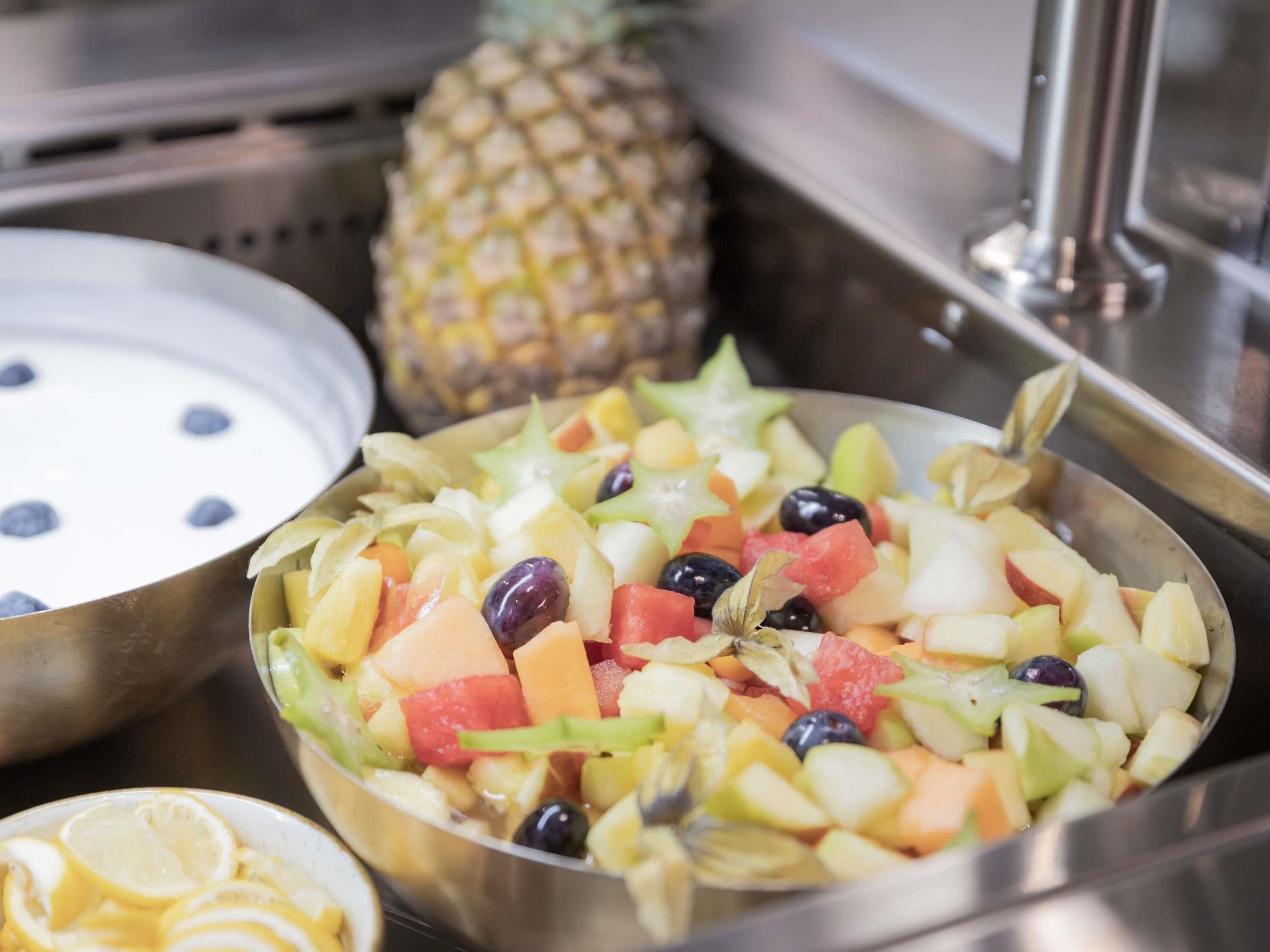 A fruit salad with various fruits and a pineapple in the background.