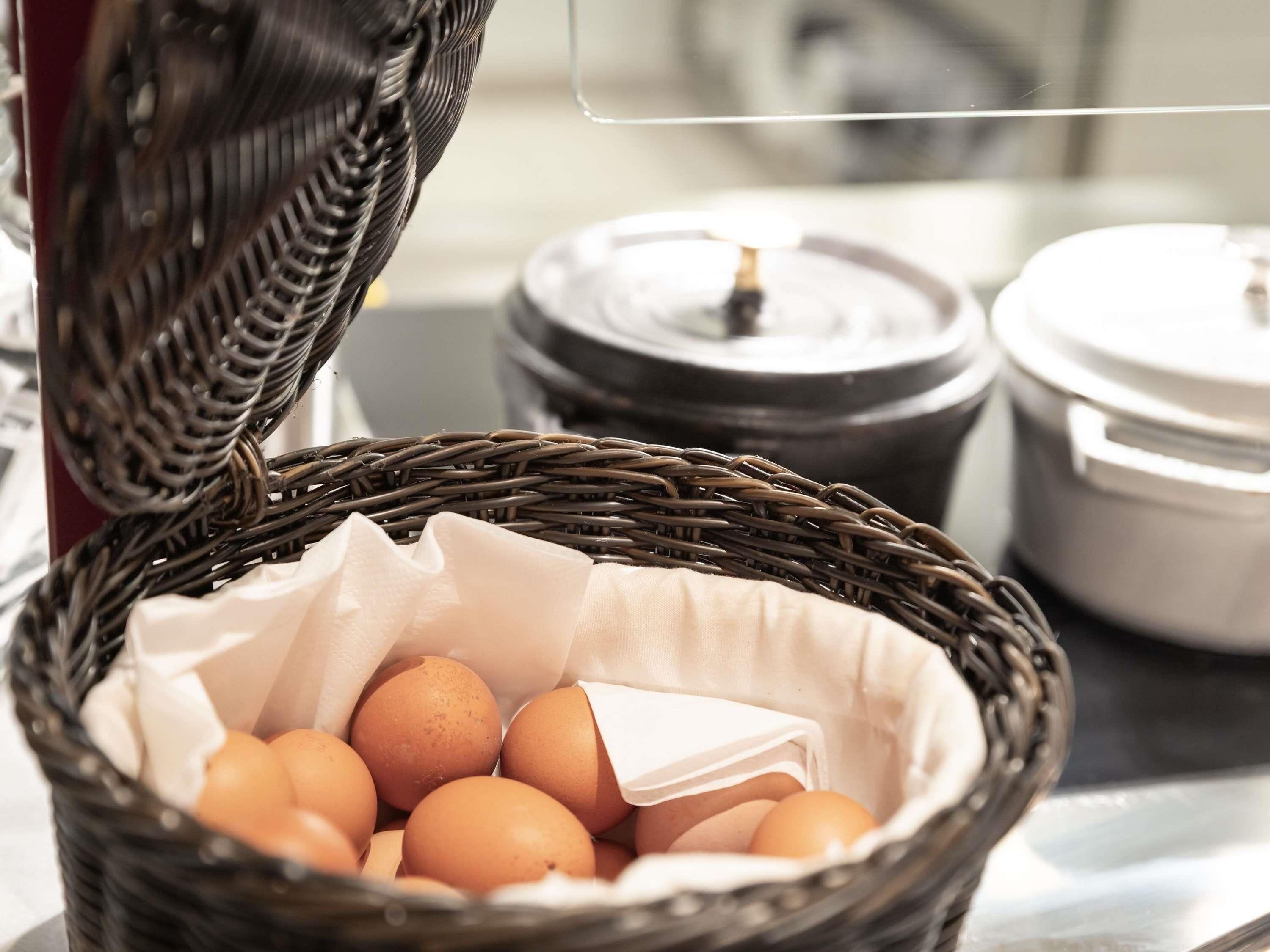 A wicker basket with eggs, a cloth, and a metal container in the background.
