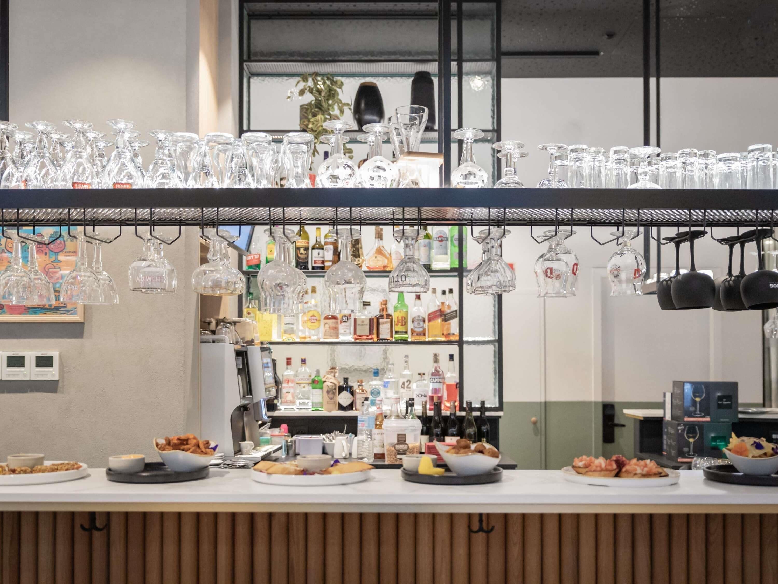 A bar area with a counter displaying food items and a variety of bottles and glasses.
