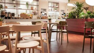 A café interior with tables and chairs, a counter with items, and hanging plants.