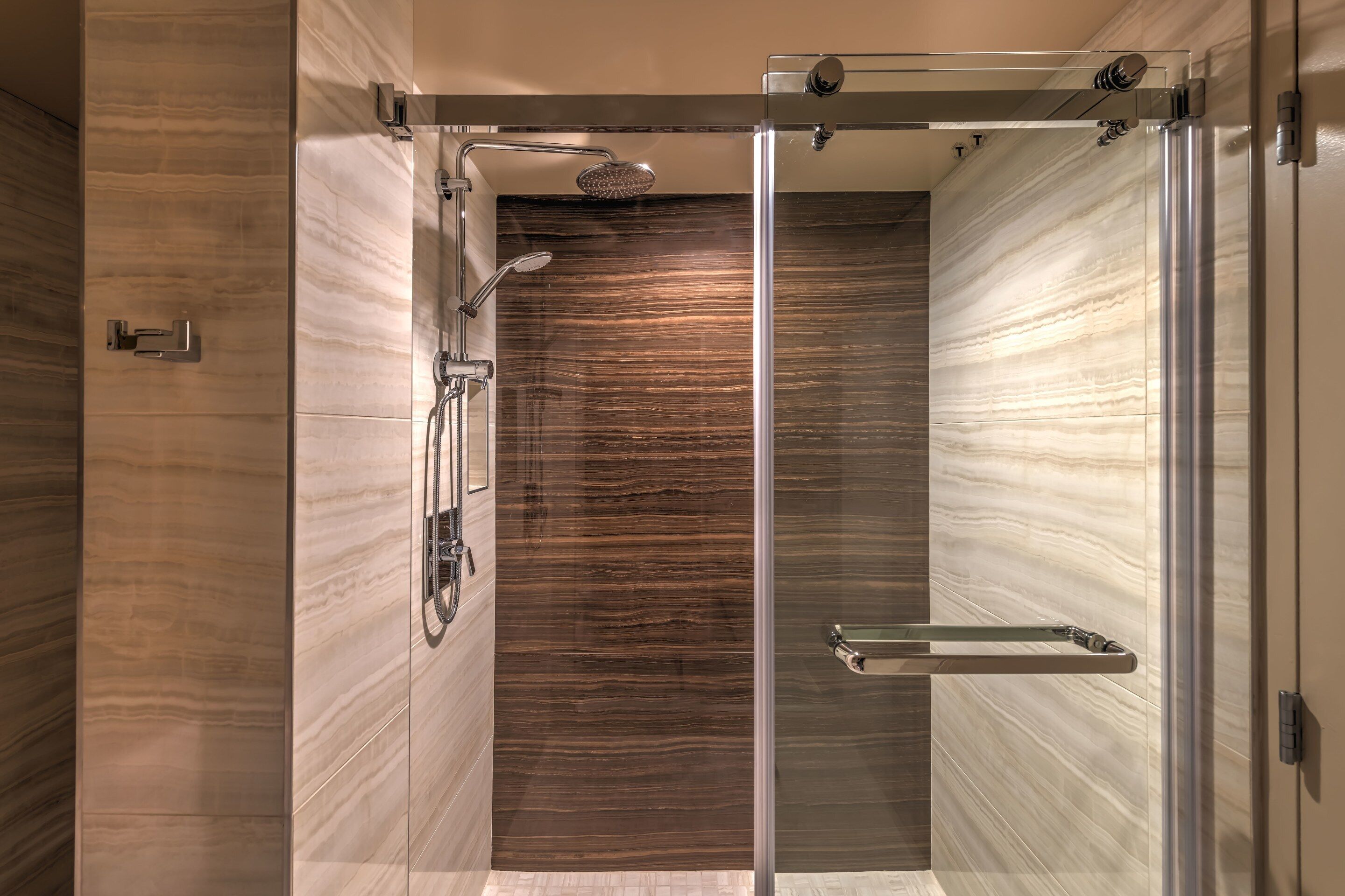A modern shower with a glass door, a handheld showerhead, and a towel rack.
