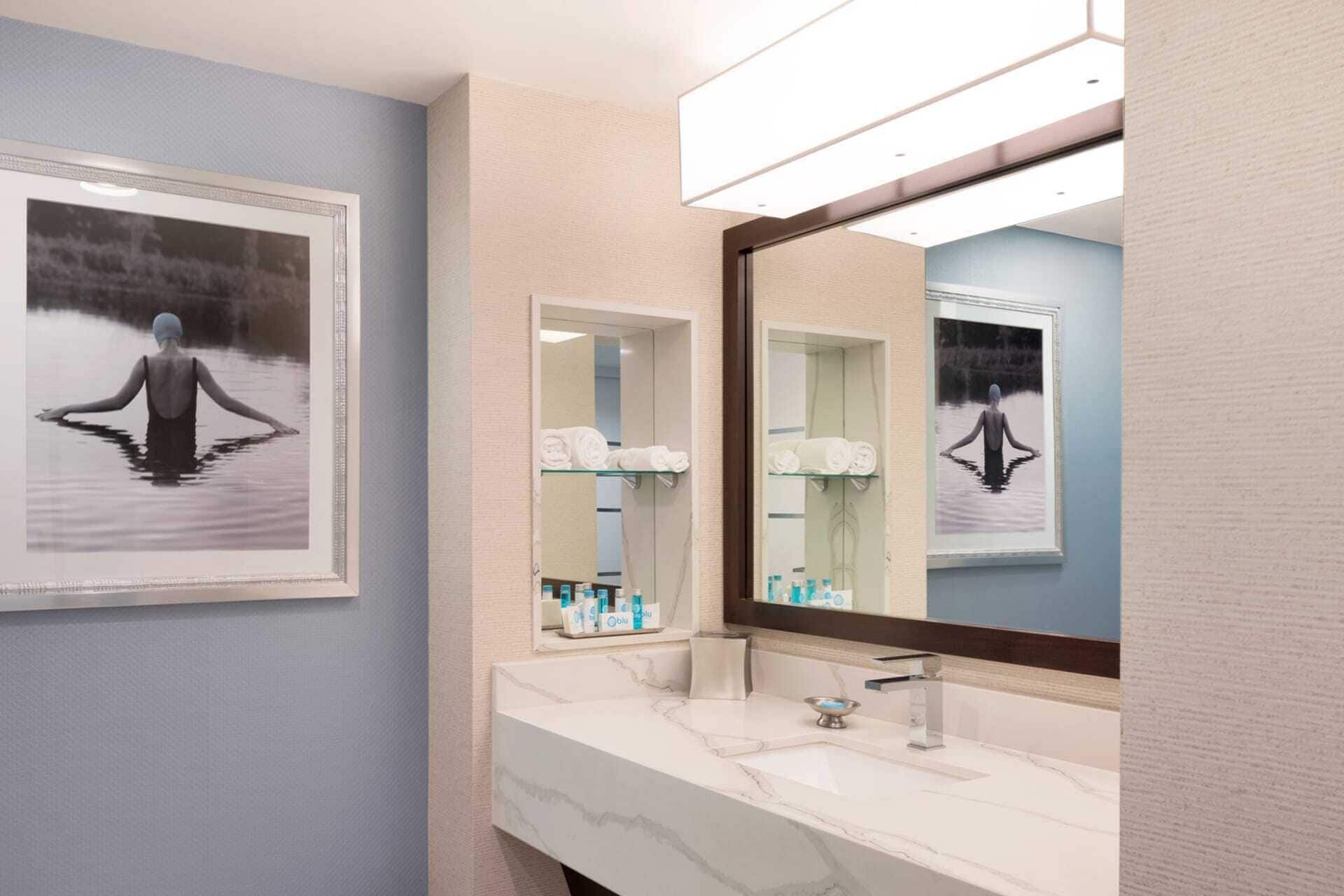 A bathroom with a marble sink, two framed pictures, a large mirror, and a shelf with toiletries.