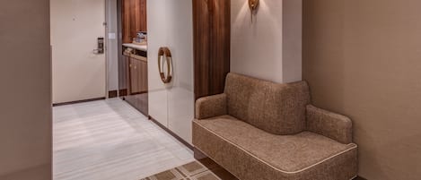 A hotel lobby with a sofa, a patterned rug, a wooden cabinet, and wall-mounted lamps.
