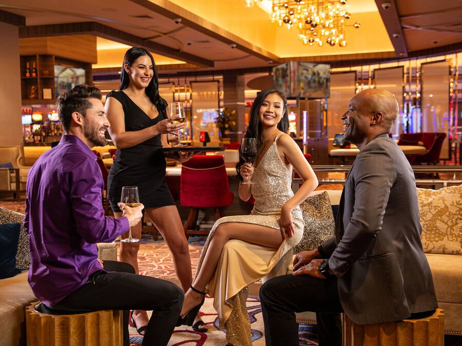 A group of people seated on stools in a well-lit, modern lounge area with a bar in the background.