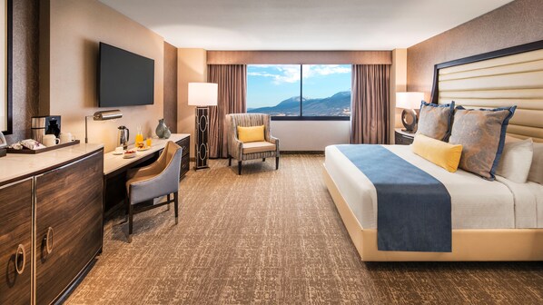 Habitación de hotel con cama, escritorio, silla y un ventanal con vista a la montaña.