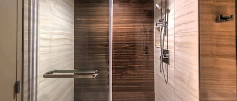 A modern shower with a glass door, a handheld showerhead, and a wall-mounted faucet.
