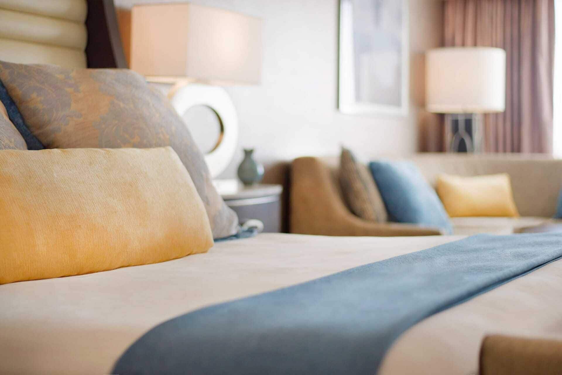 A hotel room with a bed, pillows, a lamp, and a nightstand.