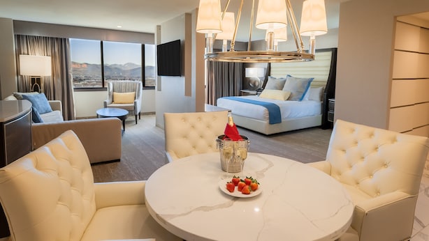 Una habitación de hotel moderna con una mesa redonda de mármol, asientos cómodos, un minibar y una cama grande con vistas a la ciudad.