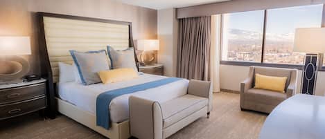 Ein Hotelzimmer mit einem großen Bett, einer Couch, einem Sessel, einem Schreibtisch und Blick auf eine Stadtlandschaft durch ein großes Fenster.