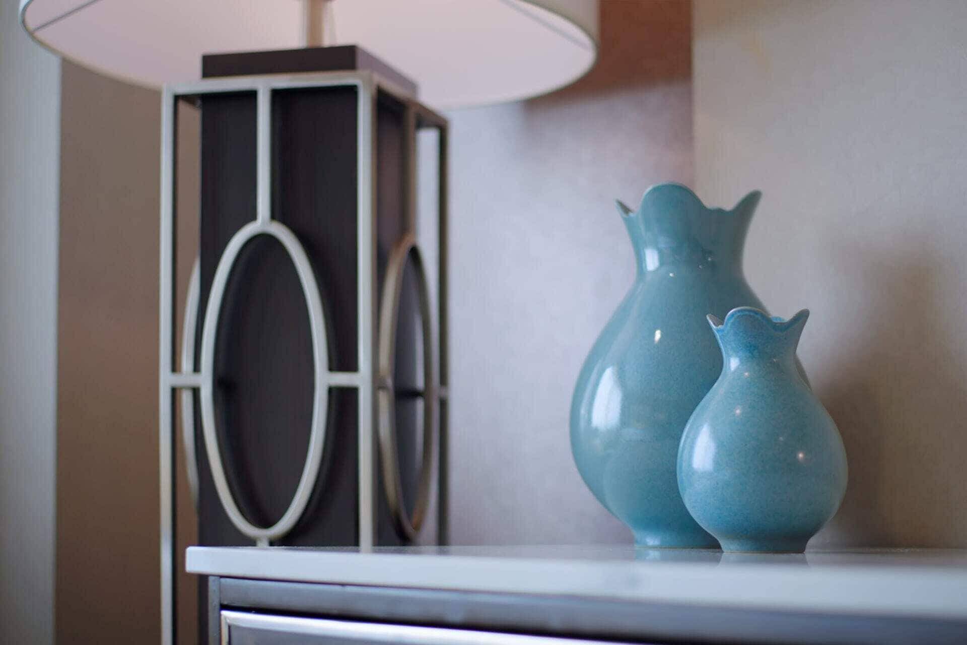 A table with two blue vases and a modern lamp.