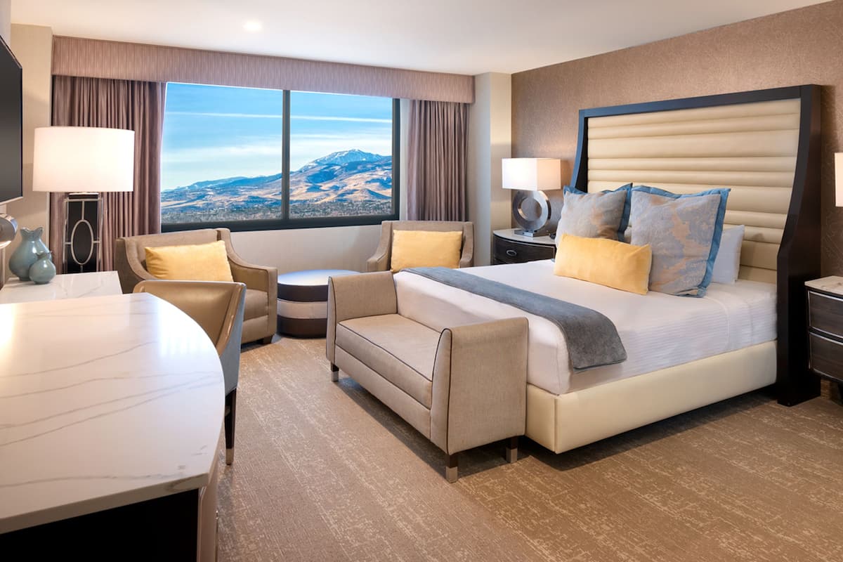 Ein Hotelzimmer mit einem großen Bett, einem Schreibtisch, einem Sessel und Blick auf einen Berg.