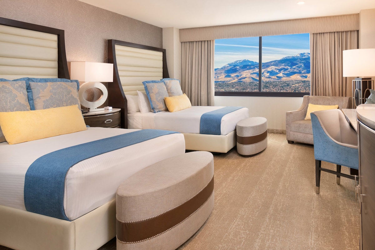 A hotel room with two beds, a sofa, a desk, and a view of mountains.